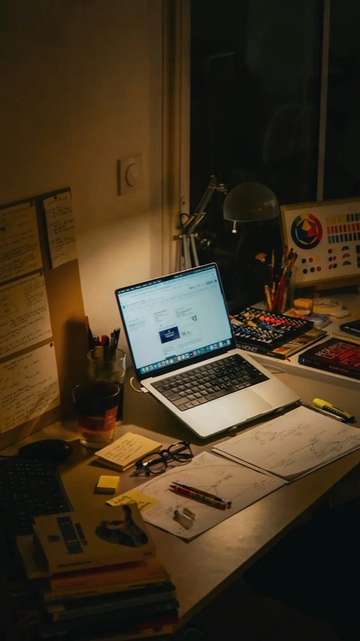 A creator's desk at night — laptop, notes and studio kit